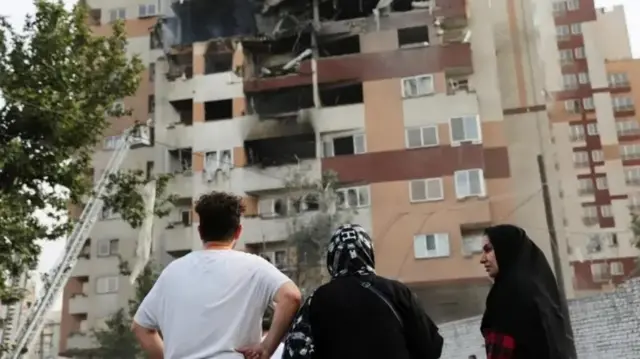 مجموعة من الأفراد يقفون أمام بناية تعرض لقصف إسرائيلي