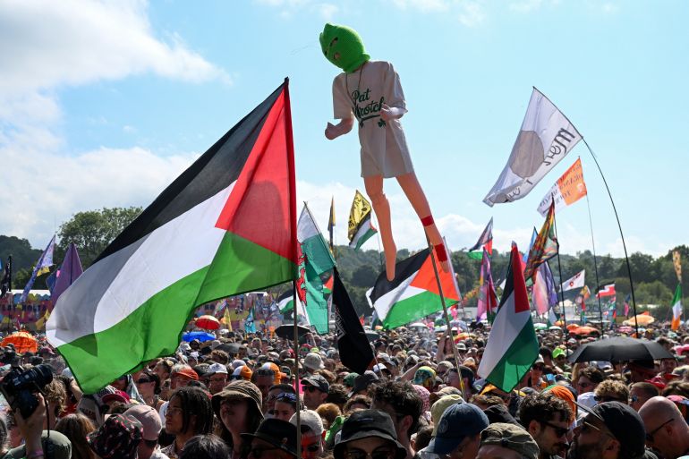 Revellers hold up Palestinian and other flags and a representation of a person wearing a balaclava on the day Kneecap performs at Glastonbury Festival at Worthy Farm in Pilton, Somerset, Britain, June 28, 2025. REUTERS/Jaimi Joy