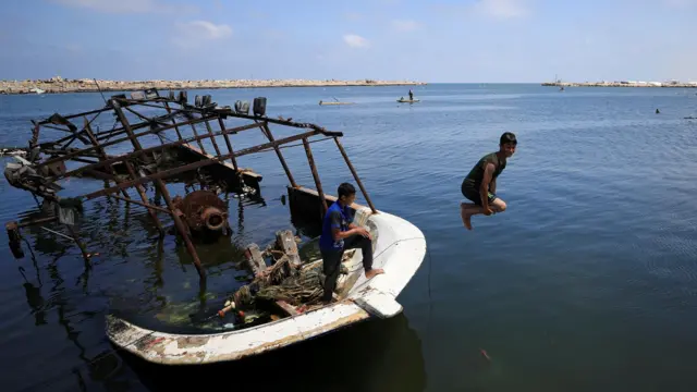 صورة لأطفال فلسطينيين في قطاع غزة يقفزون من على متن قارب محطّم إلى مياه البحر.