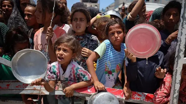 أطفال صغار يحملون أطباقاً وينتظرون المساعدات الغذائية في غزة