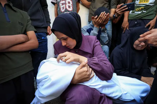 سيدة تحمل طفتلها الملفوفة في كفن أبيض