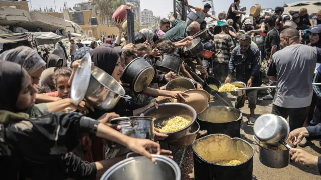 فلسطينيون يحملون أواني وينتظرون الحصول على طعام في منطقة في مدينة غزة
