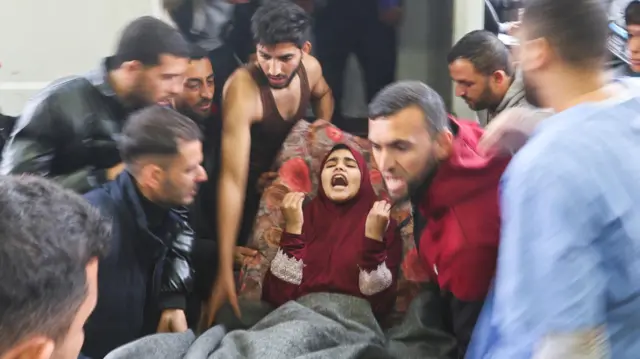 نقل جريحة فلسطينية إلى مستشفى ناصر، في أعقاب غارات إسرائيلية على مدرسة معان شرقي خان يونس، وحولها عدد من الرجال والمسعفين.