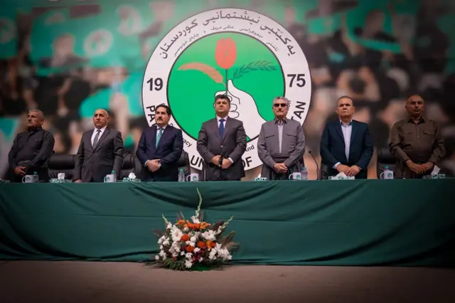 لاهور شيخ جنكي واقفاً يتوسط سبعة أشخاص، أثناء اجتماع في يوليو/تموز الماضي بمدينة السليمانية مع قادة وضباط قوات الطوارىء، ويرتدي سترة رمادية اللون وربطة عنق زرقاء بها دوائر صغيرة بيضاء وقميصاً أبيض.