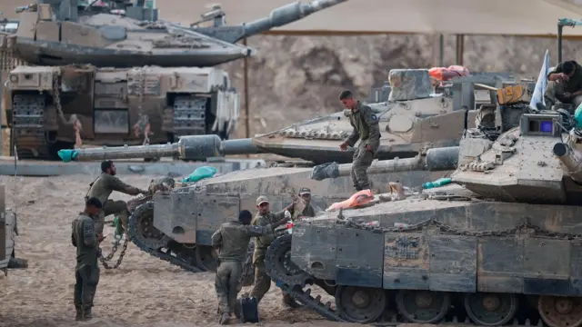 جنود إسرائيليون يقفون عند دباباتهم، واحد منهم يجلس على ظهر الدبابة وآخر يقف على ظهرها، الصورة التقطت نهاراً قرب الحدود مع غزة.