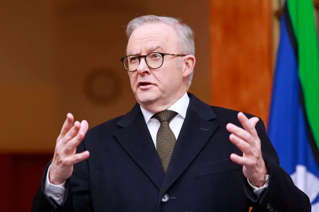 رئيس الوزراء الأسترالي أنتوني ألبانيز يتحدث خلال مؤتمر صحفي في كانبيرا في 11 أغسطس/آب 2025. يرتدي بدلة رسمية كحلية اللون ويحرك يديه أثناء حديثه وخلفه العلم الأسترالي.