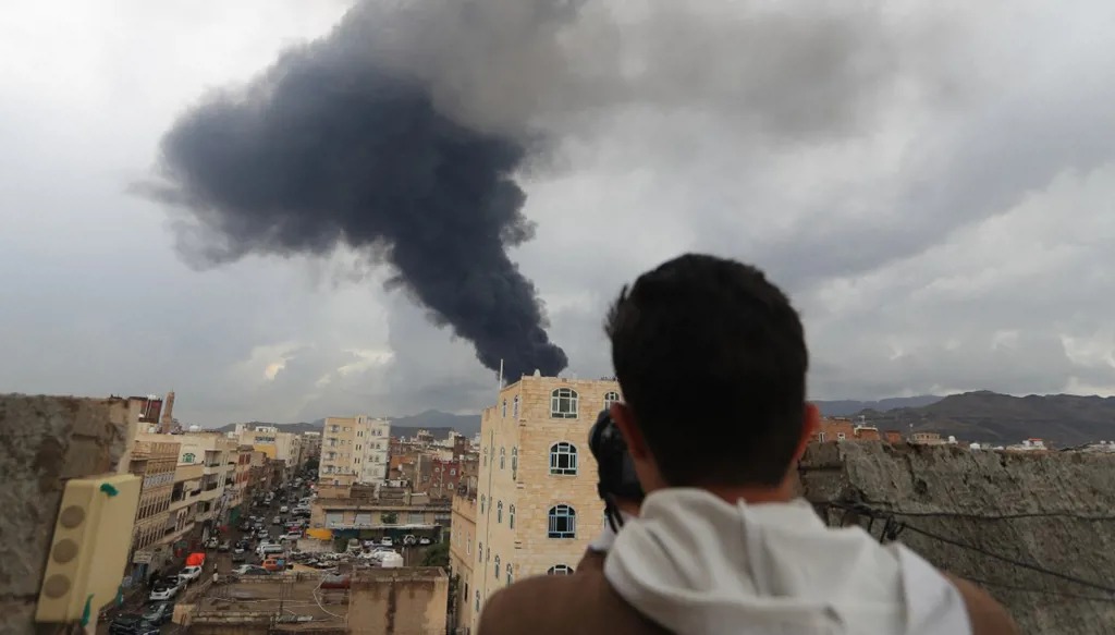 رجل يمني يلتقط صورة لدخان متصاعد جراء غارة إسرائيلية على صنعاء في 24 آب 2025. (أ ف ب)