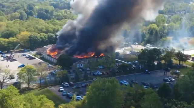 الحريق في كنيسة "يسوع المسيح لقديسي الأيام الأخيرة" بمدينة غراند بلانك الأمريكية، حيث تظهر ألسنة اللهب وسُحب الدخان تتصاعد من الكنيسة، بينما تنتشر سيارات الشرطة والإسعاف حول المكان.