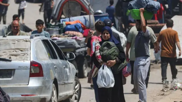 فلسطينيون يحملون أمتعتهم ويسيرون يجانب سيارات مدمرة في قطاع غزة