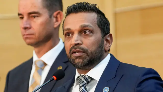 مدير مكتب التحقيقات الفيدرالي كاش باتيل يتحدث خلال المؤتمر الصحفي. يظهر بلحية خفيفة مرتدياً سترة زرقاء وقميصاً أبيض وربطة عنق منقوشة بدرجات الرمادي والأسود والأبيض.