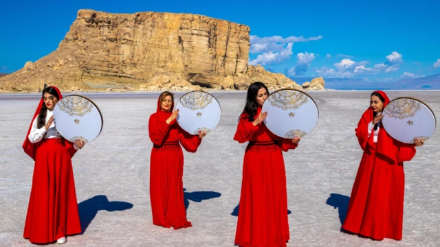 أربع نساء إيرانيات يرتدين زياً أحمر اللون وبأيديهن دفوف بينما يقفن على قاع بحيرة أرومية يوم 11 أبريل/نيسان 2023، في محاولة للفت الأنظار إلى آثار التغير المناخي 