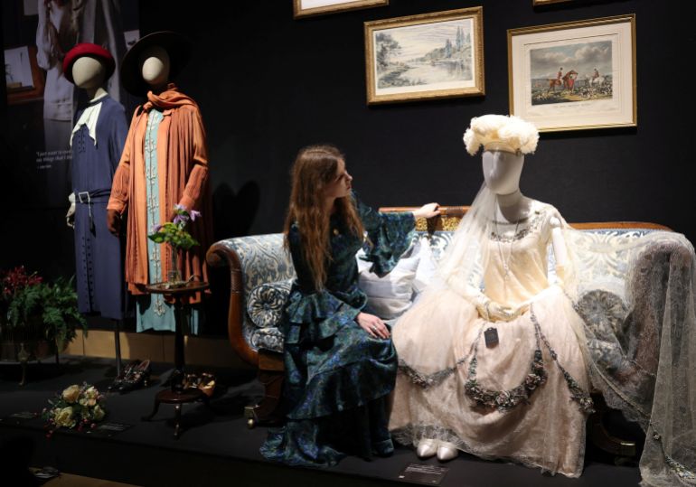 A gallery assistant poses with a presentation dress worn by actress Lily James (as Lady Rose) in season 4, episode 9, during a press preview for the Downton Abbey farewell exhibition and an auction of props, costumes, and set pieces at Bonhams in London, Britain, August 18, 2025. REUTERS/Hannah McKay