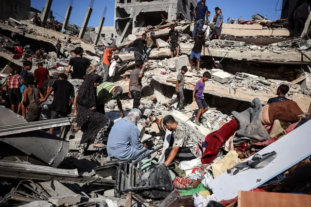 فلسطينيون يبحثون عن أشياء قابلة للإنقاذ وسط أنقاض منازل مدمرة انهارت بعد لحظات من قصفها بغارة جوية إسرائيلية في اليوم السابق، في مدينة غزة، 12 سبتمبر/أيلول 2025.