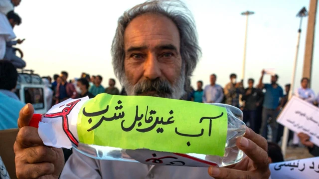 إيراني يحمل زجاجة مياه مكتوب عليها "تحذير: مياه غير صالحة للشرب" – ضمن مظاهرة احتجاجية خرجت في محافظة سيستان-بلوشستان الإيرانية يوم 31 يوليو/تموز 2023 بسبب أزمة المياه