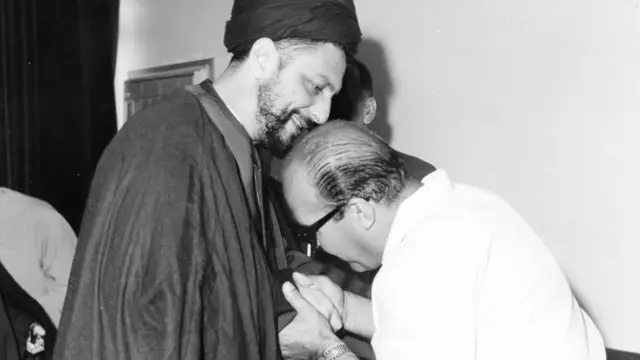 الصدر مع شخص يبدو أنه ينحني ليقبل يديه