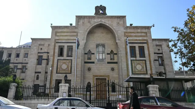 أشخاص يسيرون أمام مبنى البرلمان في العاصمة دمشق، في 14 ديسمبر/كانون الأول 2024.