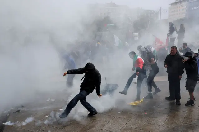 صورة تظهر انتشار الغاز المسيل للدموع في أحد الشوارع التي تشهد مظاهرات في إيطاليا، أحد المتظاهرين يرتدي علماً فلسطينياً
