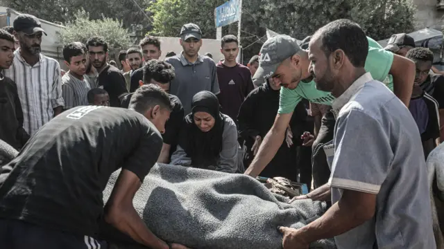 يحمل فلسطينيون جثمان ضحية إلى مستشفى العودة في مخيم النصيرات للاجئين بعد أن أطلقت القوات الإسرائيلية النار على مدنيين ينتظرون المساعدة على طول ممر نتساريم في قطاع غزة في 2 سبتمبر/أيلول 2025.