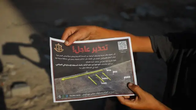 يد ممسكة بمنشور ألقاه الجيش الإسرائيلي على سكان مدينة غزة لمطالبتهم بالإخلاء
