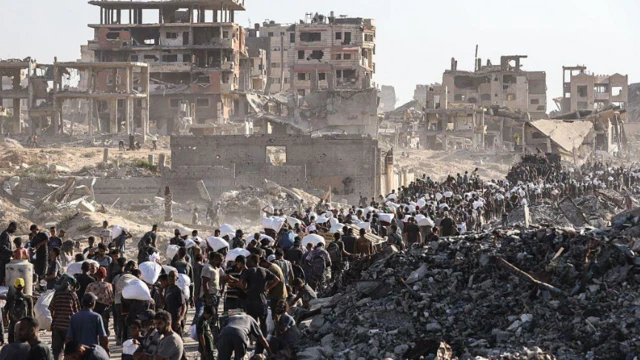 جموع من الفلسطينيين عند مركز لتوزيع المساعدات قُرب معبر زيكيم الحدودي، تحيط بهم أنقاض مبانٍ تعرّضتْ للتفجير.