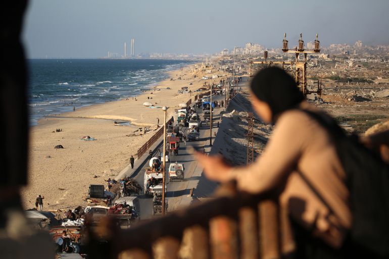 A woman watches from a balcony as Palestinians flee south from Gaza City with their belongings, via the coastal road near the Nuseirat refugee camp in the central Gaza Strip, on September 12, 2025.
