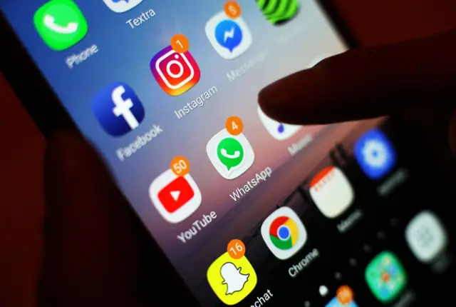 صورة تظهر شخصاً يمرر إصبعه فوق شاشة هاتفه المثبت عليه عدد من وسائل التواصل الاجتماعي.