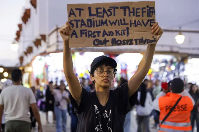 شاب يحمل لافتة مكتوب عليها: على الأقل ملاعب الفيفا ستحصل على حقيبة إسعاف أولي، فيما لا تملك مستشفيتنا ذلك