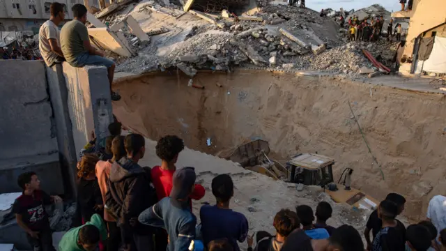 يتجمّع عدد من السكان المحليين لمتابعة أعمال حفّارة في موقع بمدينة حمد في خان يونس جنوبي قطاع غزة، حيث تواصل كتائب القسام، الجناح العسكري لحركة حماس، عمليات البحث عن جثث رهائن إسرائيليين، وذلك في 17 تشرين الأول/أكتوبر 2025.