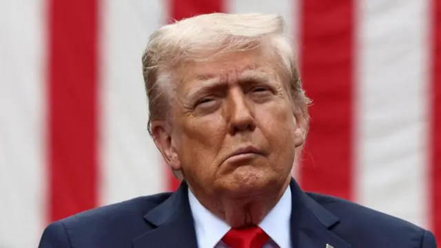 دونالد ترامب مرتديا بذلة وكرافت أحمر وخلفه علم الولايات المتحدة الأمريكية