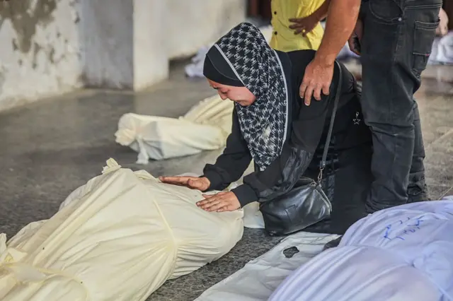 سيدة فلسطينية تنحني أمام جثة أحد أقاربها بجوار جثث أخرى قبل تشييعها