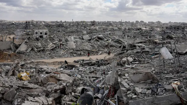 فلسطينيون يسيرون بين أنقاض مبانٍ مدمرة في حي في مدينة غزة، بعد سريان وقف إطلاق النار وانسحاب القوات الإسرائيلية من أجزاء من قطاع غزة.