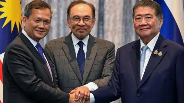 أنور (في الوسط)، ورئيس الوزراء الكمبودي هون مانيت (على اليسار)، ورئيس الوزراء التايلاندي بالنيابة فومثام ويتشاياشاي محادثات السلام في كوالالمبور في يوليو/تموز وجميعهم يرتدون بدلات رسمية ويضعون أيديهم فوق بعضها البعض.