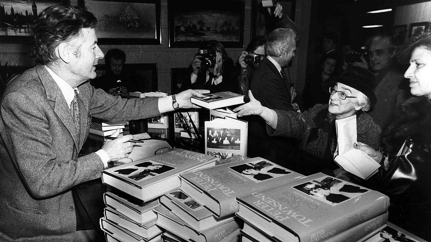 بيتر تاونسند خلال توقيع نسخ من مذكراته في حفل إطلاق كتابه بلندن عام 1978، وهو يسلّم إحدى النسخ لامرأة من الجمهور بينما تلتقط الكاميرات اللحظة في مشهد يعكس استمرار الاهتمام بقصته مع الأميرة مارغريت بعد عقود من نهايتها.