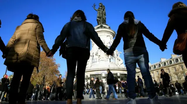 أشخاص يمسكون أيدي بعضهم البعض تضامنا مع ضحايا هجمات باريس 2015 أمام مبنى مسرح الباتاكلان في برايس