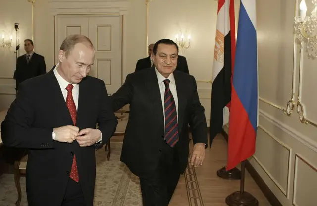 الرئيس المصري حسني مبارك والرئيس الروسي فلاديمير بو يسيران بجوار بعضهما البعض ويرتدي كل منهما سترة سوداء وسرولاً أسود وقميصاً أبيض بعد محادثات في مقر إقامتهما في نوفو- أوغاريفو خارج موسكو في 25 مارس/آذار 2008.