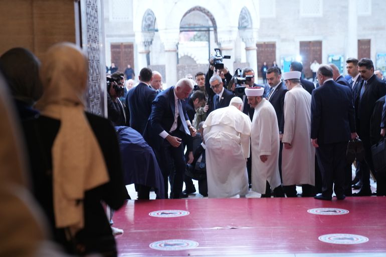 Pope Leo XIV, center, puts his shoes back on after visiting the Ottoman-era Sultan Ahmed or Blue Mosque, in Istanbul, Turkey, Saturday, Nov. 29, 2025. (AP Photo/Domenico Stinellis)