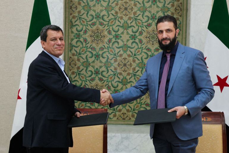 A handout picture released by the official Syrian Arab News Agency (SANA) shows Syria's interim president Ahmed al-Sharaa (R) shaking the hand of Syrian Democratic Forces (SDF) commander-in-chief Mazloum Abdi after the signing of an agreement, to integrate the institutions of the semi-autonomous Kurdish administration in the northeast into the national government, in the Syrian capital Damascus on March 10, 2025. (Photo by SANA / AFP) / == RESTRICTED TO EDITORIAL USE - MANDATORY CREDIT "AFP PHOTO / HO / SANA" - NO MARKETING NO ADVERTISING CAMPAIGNS - DISTRIBUTED AS A SERVICE TO CLIENTS ==
