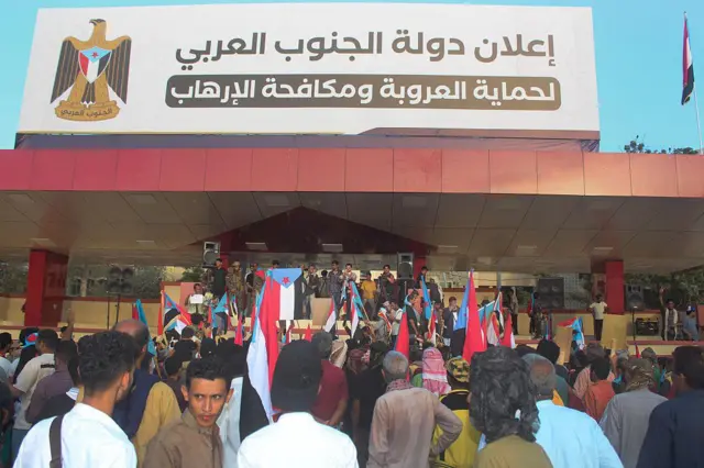 مجموعة من أنصار المجلس الانتقالي الجنوبي في عدن يرفعون علم "جمهورية اليمن الديمقراطية الشعبية" القديم وفوق المنصة لائحة كتب عليها: "إعلان دولة الجنوب العربي لحماية العروبة ومكافحة الإرهاب".