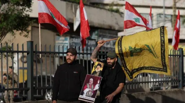شخصان يرفعان راية لحزب الله وأمينها العام الراحل حسن نصر الله بالإضافة إلى صورة للبابا