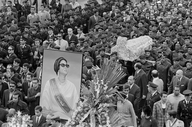 صورة تظهر مواطنين مصريين، ورجال أمن يسرون في جنازة عسكرية أُقيمت لأم كلثوم عام 1975.ويحمل ضباط نعش المطربة المصرية الراحلة، بينما يسر آخرون، حاملين صورة لها.
