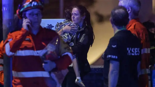 سيدة تحمل طفلاً ملفوفاً ببطانية بعد حادثة إطلاق نار على شاطئ بونداي في سيدني في 14 ديسمبر/كانون الأول 2025