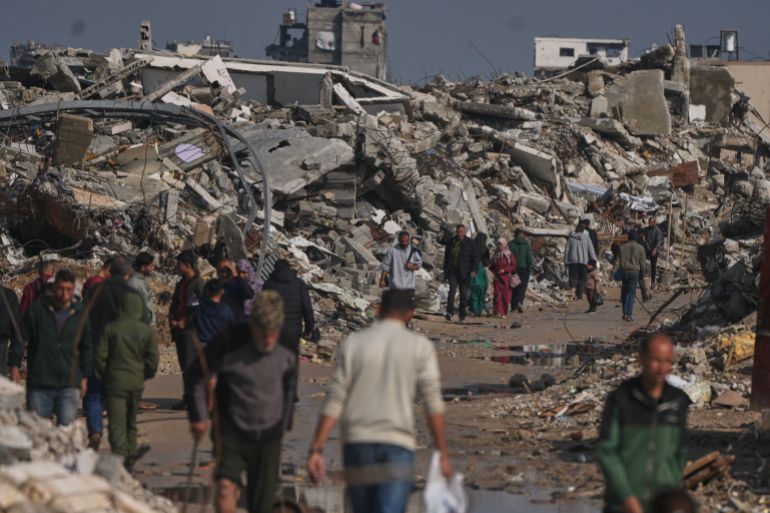 Palestinians walk along a street surrounded by buildings destroyed during Israeli air and ground operations in Gaza City, Wednesday, Dec. 17, 2025. (AP Photo/Jehad Alshrafi)