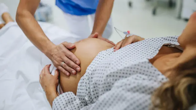 طبيبة نسائية تفحص امرأة حامل في المستشفى، تلمس بطنها، وتفحص وضعية الجنين، ووضعية المقعدة، وحجمه، وحركاته. امرأة في حالة مخاض مستلقية على سرير المستشفى، تتحدث مع طبيبة نسائية في جناح الولادة.