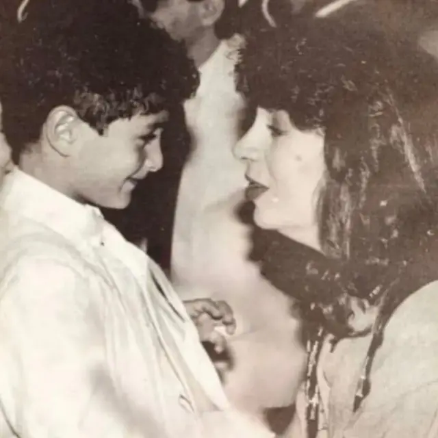 الفنانة سمية الألفي تنظر وتبتسم لنجلها أحمد الفيشاوي عندما كان طفلاً، بينما ينظر هو إليها ويبادلها أيضاً ابتسامة.