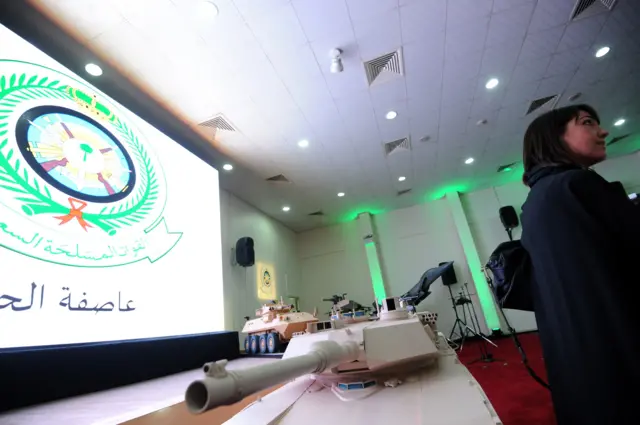 صحفي أجنبي يقف إلى جانب مجسّم لدبابة تابعة للقوات المسلحة الإماراتية خلال إحاطة إعلامية لعملية "عاصفة الحزم" في قاعدة جوية بالرياض، أبريل 2015.