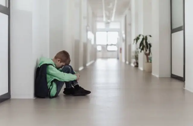 طفل يجلس على الأرض داخل أحد الممرات ويضع رأسه بين رجليه