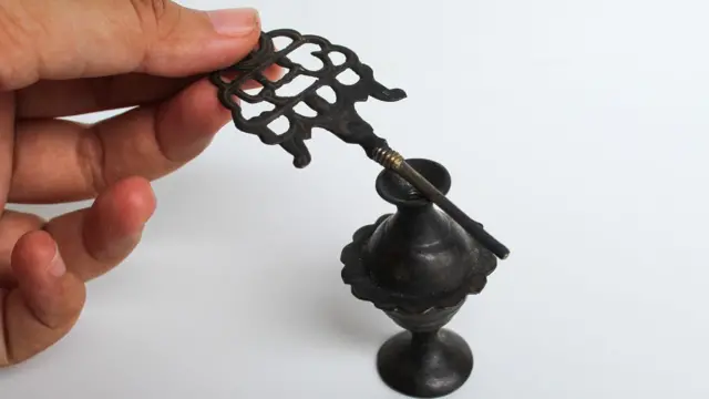 يد امرأة تمسك أداة قديمة لوضع كحل العيون، إلى جانب وعاء قديم مخصص لحفظ الكحل.