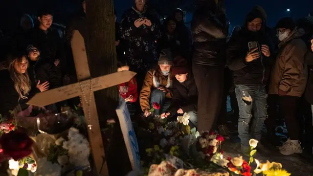 يتجمع الناس عند نصب تذكاري لـ"غود". هناك شموع وزهور وصليب كبير.