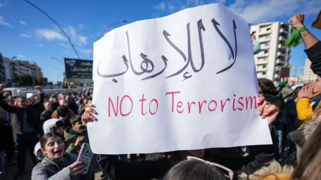 متظاهر يحمل لافتة بينما يتجمع أفراد من الطائفة العلوية للاحتجاج على العنف ضد العلويين في أعقاب تفجير مسجد حمص، في مدينة اللاذقية، سوريا، 28 ديسمبر 2025.