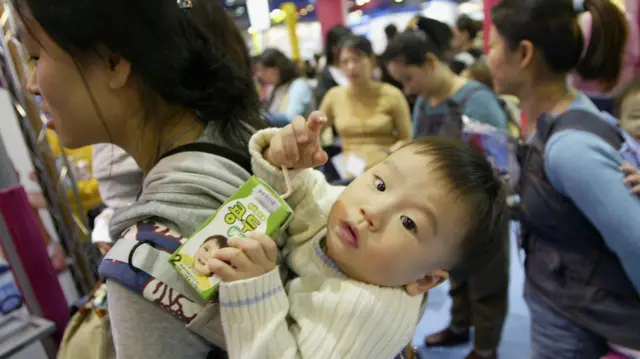 شابة كورية تحمل طفلها على ظهرها ويمسك في يده مشروب للأطفال